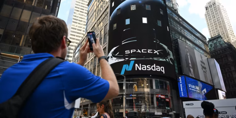 A person filming the SpaceX and Nasdaq logos on a large screen in Times Square