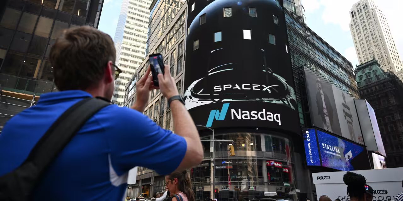 A person filming the SpaceX and Nasdaq logos on a large screen in Times Square