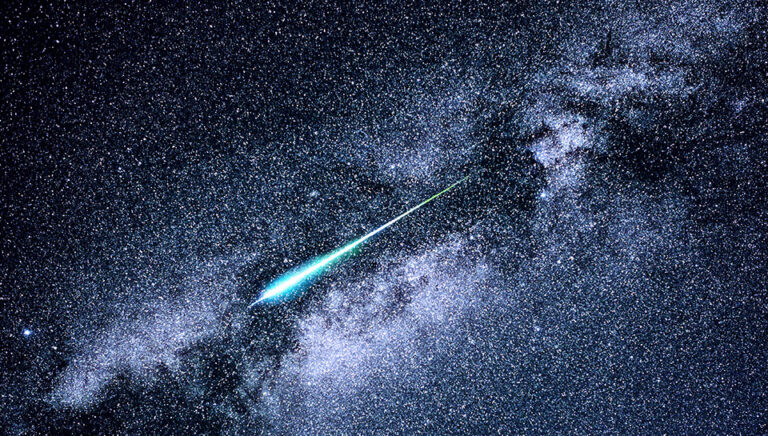 An image of a meteor with a blue trail streaking across a starry night sky