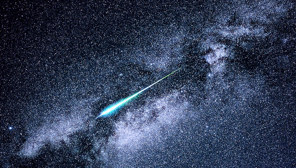 An image of a meteor with a blue trail streaking across a starry night sky