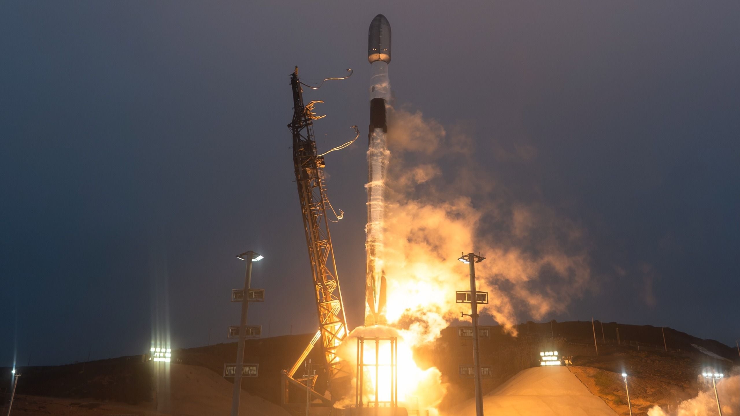 a black and white rocket launches into a darkening evening sky