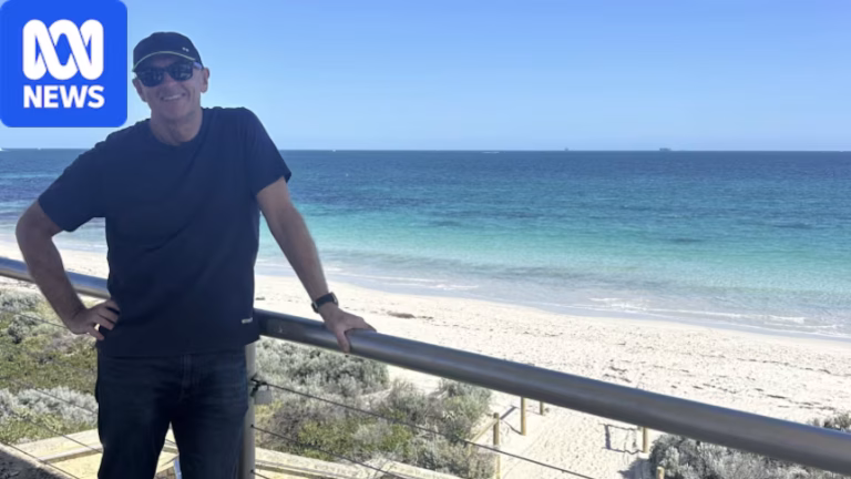 A man wears sunglasses and a hat as he stands by the beach