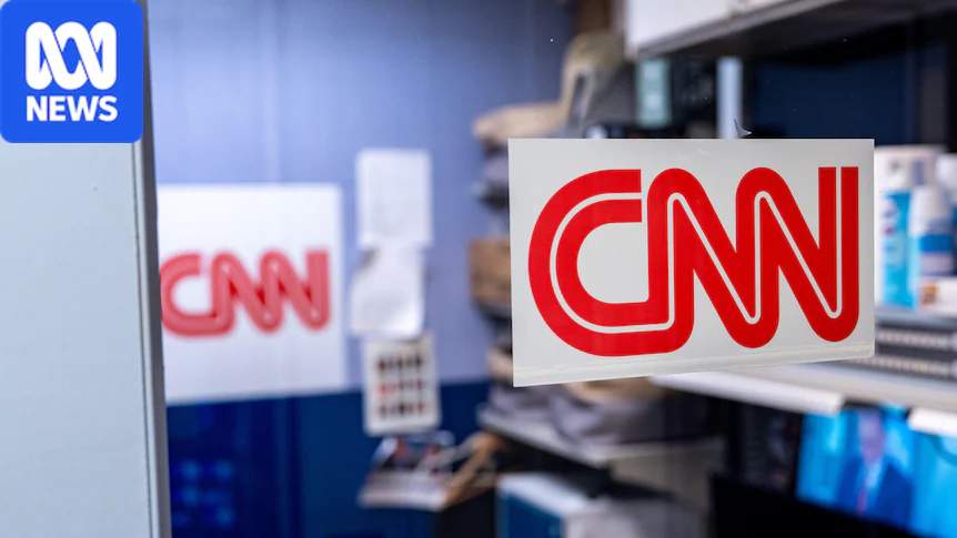 A sign with the CNN logo posted on a glass wall, with a desk behind it