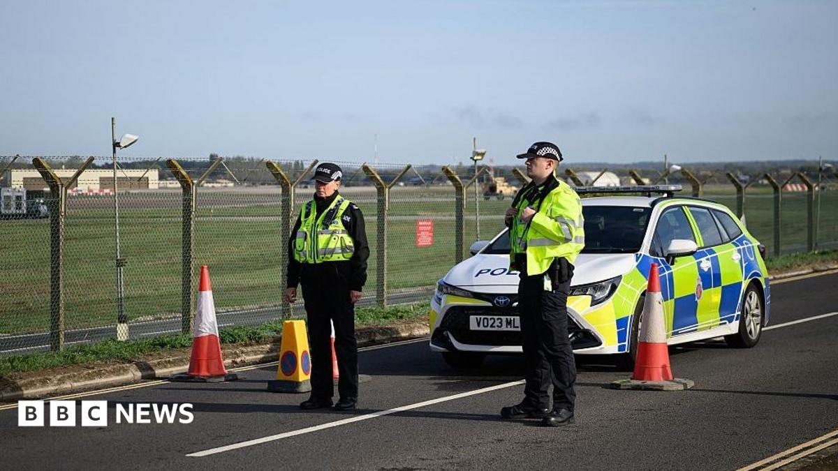 Two police officers stand with a police car outside RAF Fairford